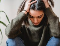 depressed young ethnic lady touching head and looking down sitting near wall
